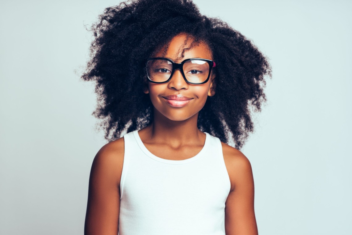 Cute youing African girl wearing glasses against a gray backgrou