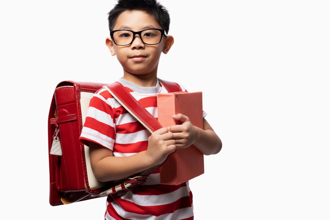 Happy cute clever boy in glasses with school bag and book in his
