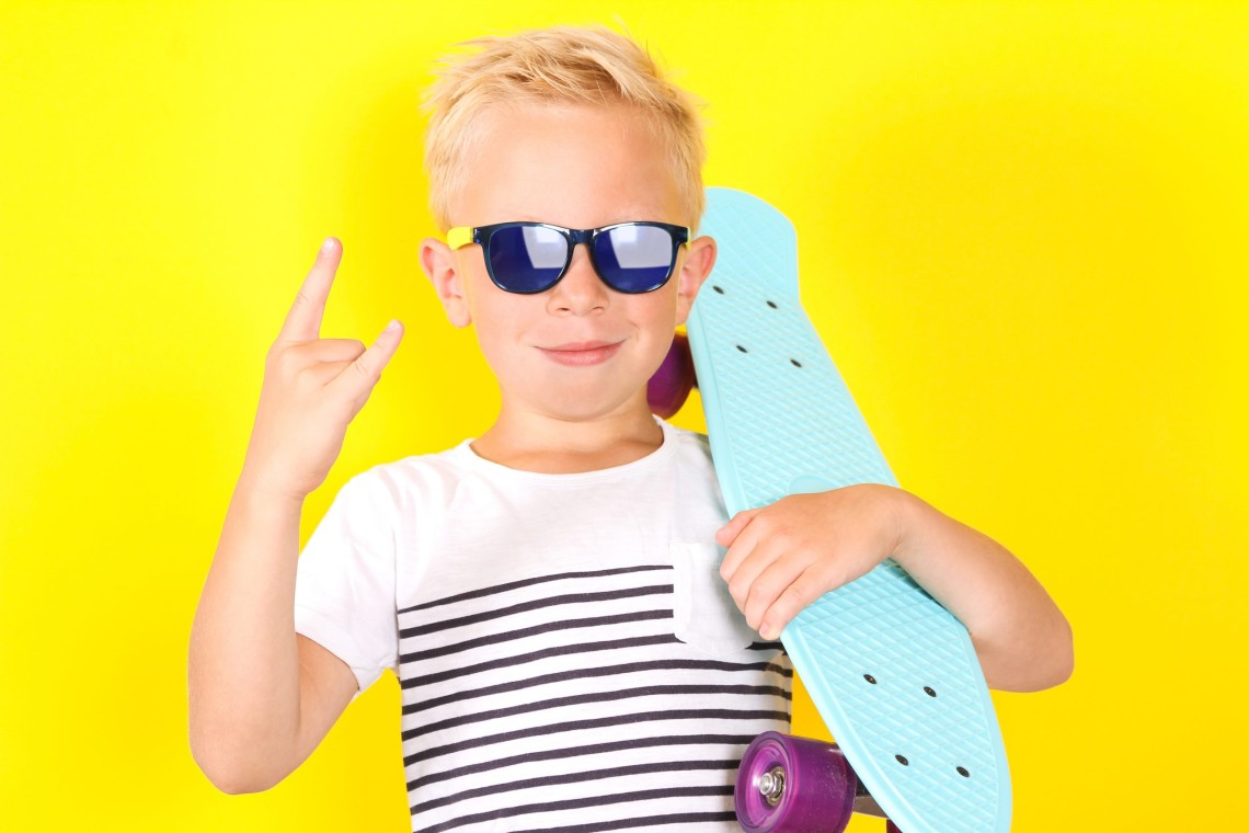 Cute cool blond boy wearing sunglasses with skateboard in his arms